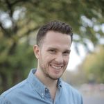 A smiling man in a denim shirt enjoying a sunny day outdoors.